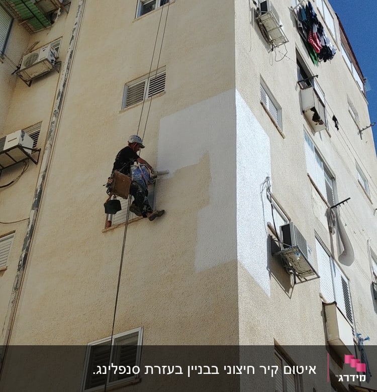 אדם צובע קיר חיצוני של בניין גבוה